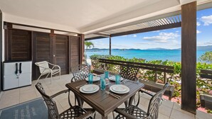 Un comedor con una mesa dispuesta para dos personas, vista al mar y un espacio exterior cubierto con un banco de madera.