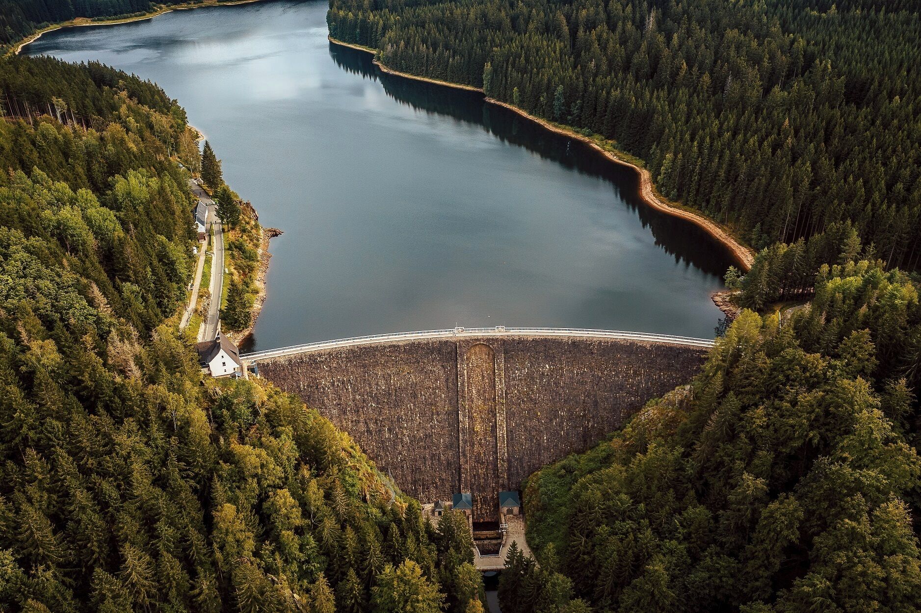 Suuri pato, jonka päällä kulkee silta järven yllä, ja jonka ympärillä on tiheää metsää.