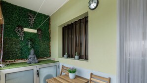A room with a green wall, a window with blinds, a small table with a plant, and a statue.