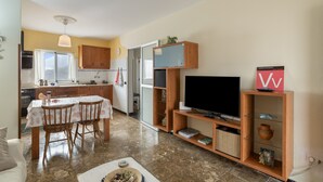 A compact living space with a dining area, kitchenette, and a TV on a wooden stand.
