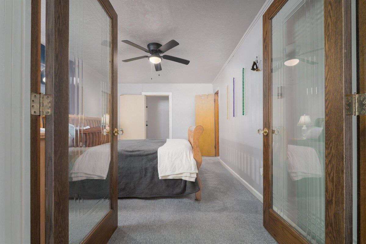 Une chambre à coucher avec un lit, un ventilateur de plafond et une porte donnant sur une autre pièce.