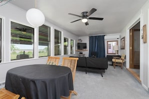 A room with a dining table, chairs, a sofa, a television, and a ceiling fan.