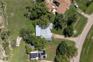 An aerial view of a property with a large house, solar panels, and surrounding greenery.