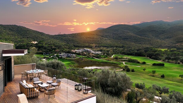 A deck with outdoor furniture overlooking a golf course and a lake, with buildings in the background. - Argentario Golf Villas (Monte Argentario)