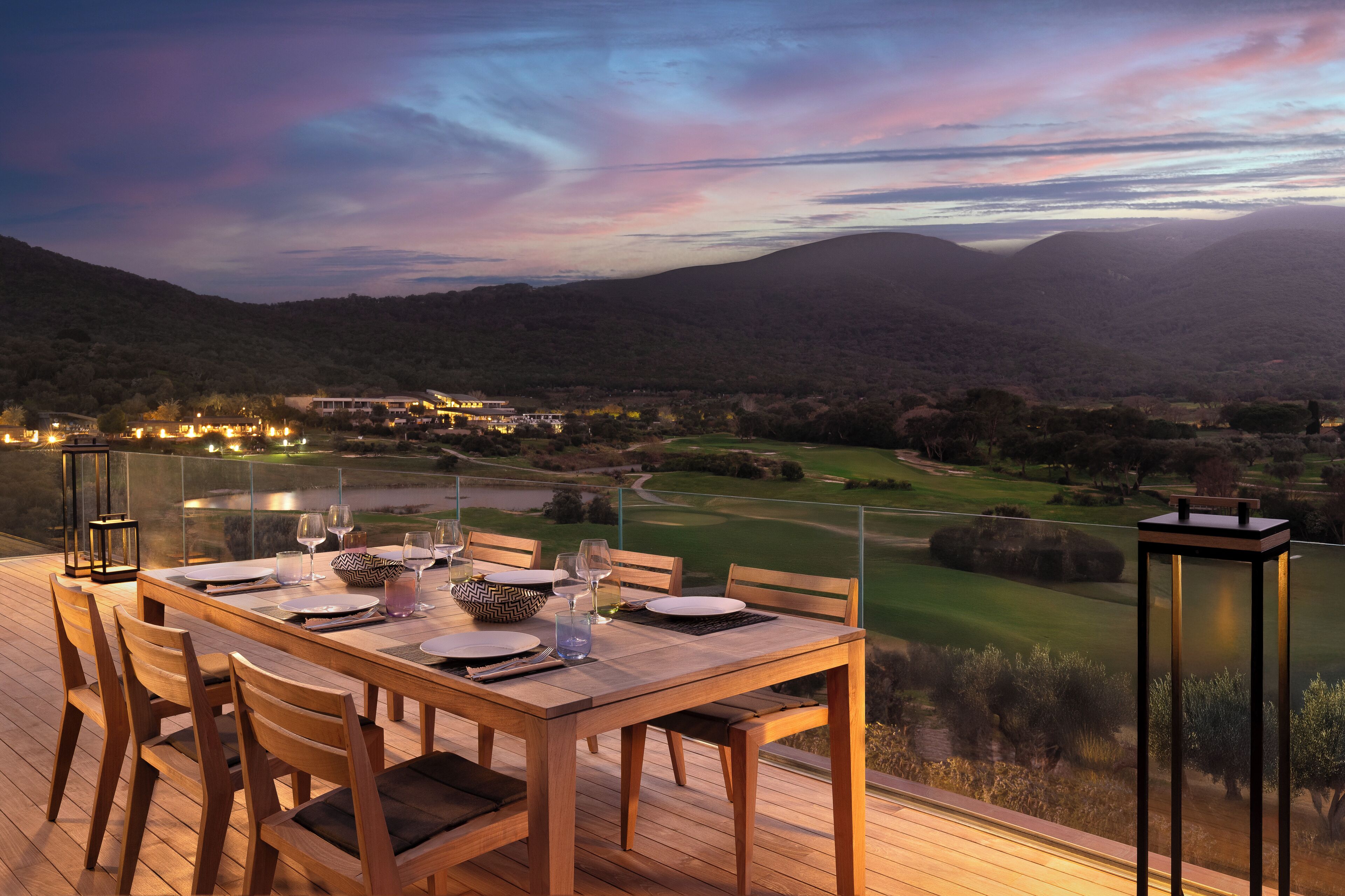A dining table set for four with a scenic view of a golf course and mountains in the background.