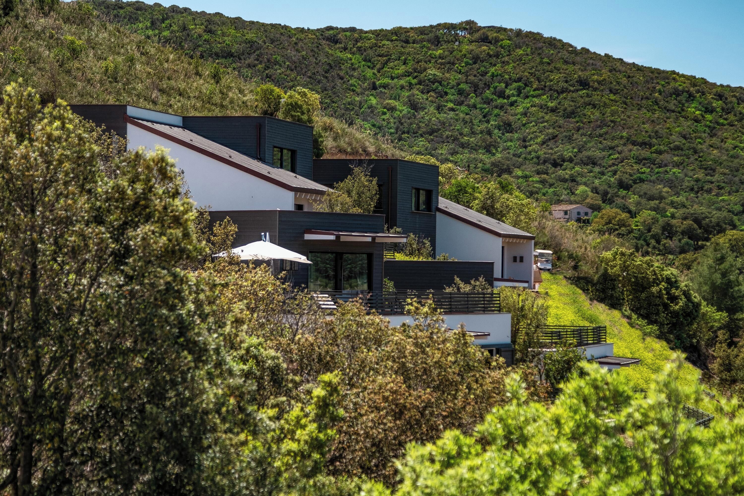 A modern house with a flat roof, surrounded by lush greenery and hills.