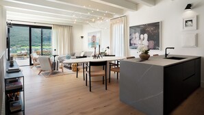 A modern living space with a dining area, kitchen, and large windows offering a view of the outdoors. - Argentario Golf Villas (Monte Argentario)