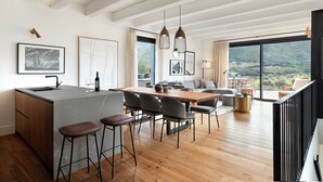 A modern kitchen with a central island, bar stools, and a dining area with chairs. - Argentario Golf Villas (Monte Argentario)
