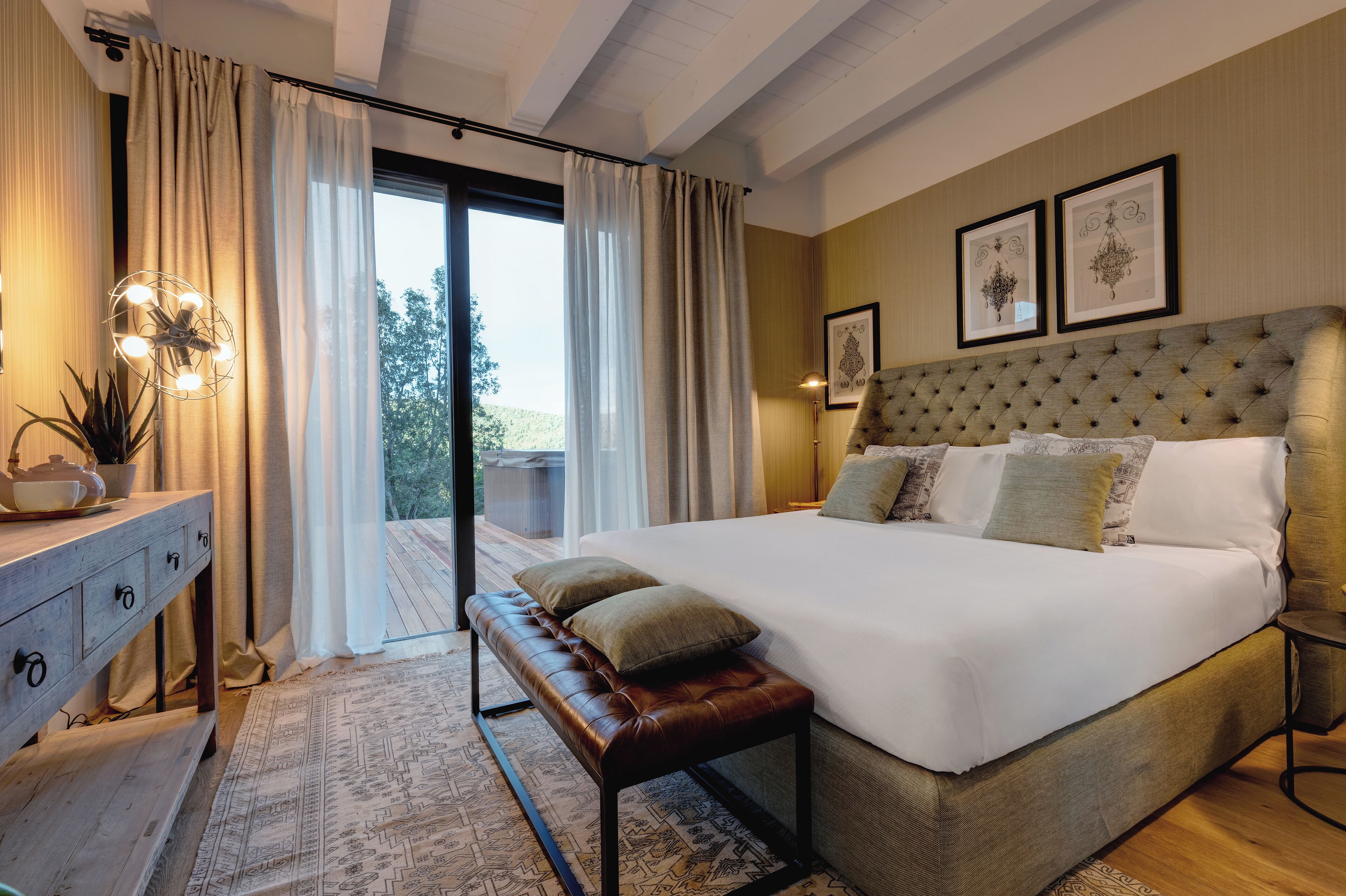 A spacious bedroom with a large bed, a bench, a bedside table, and a view through a glass door.