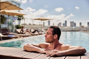 Ein Mann entspannt am Pool, im Hintergrund liegen Liegestühle und Sonnenschirme.
