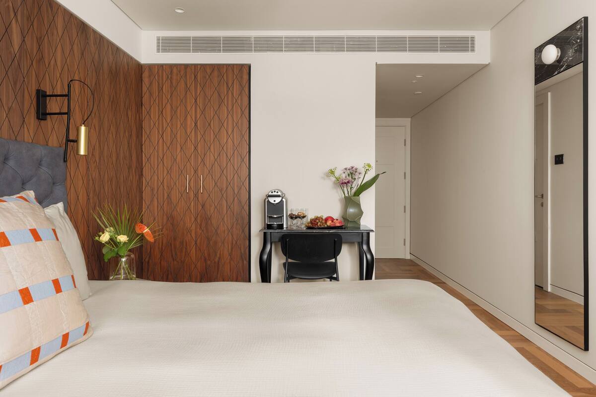 A modern bedroom with a bed, a desk, and a mirror.