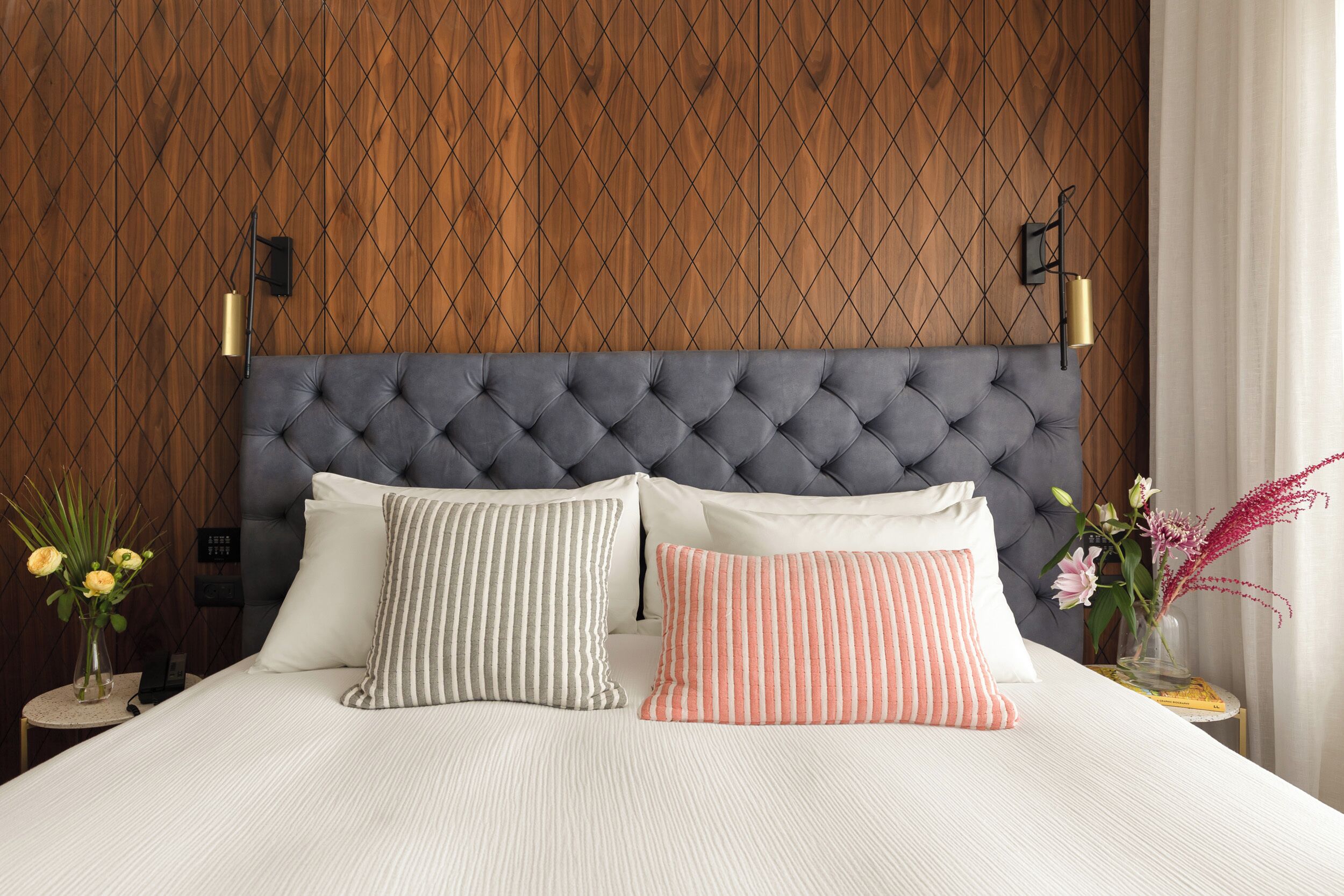 A neatly made bed with a tufted headboard, two pillows, and a bedside table with a vase of flowers.