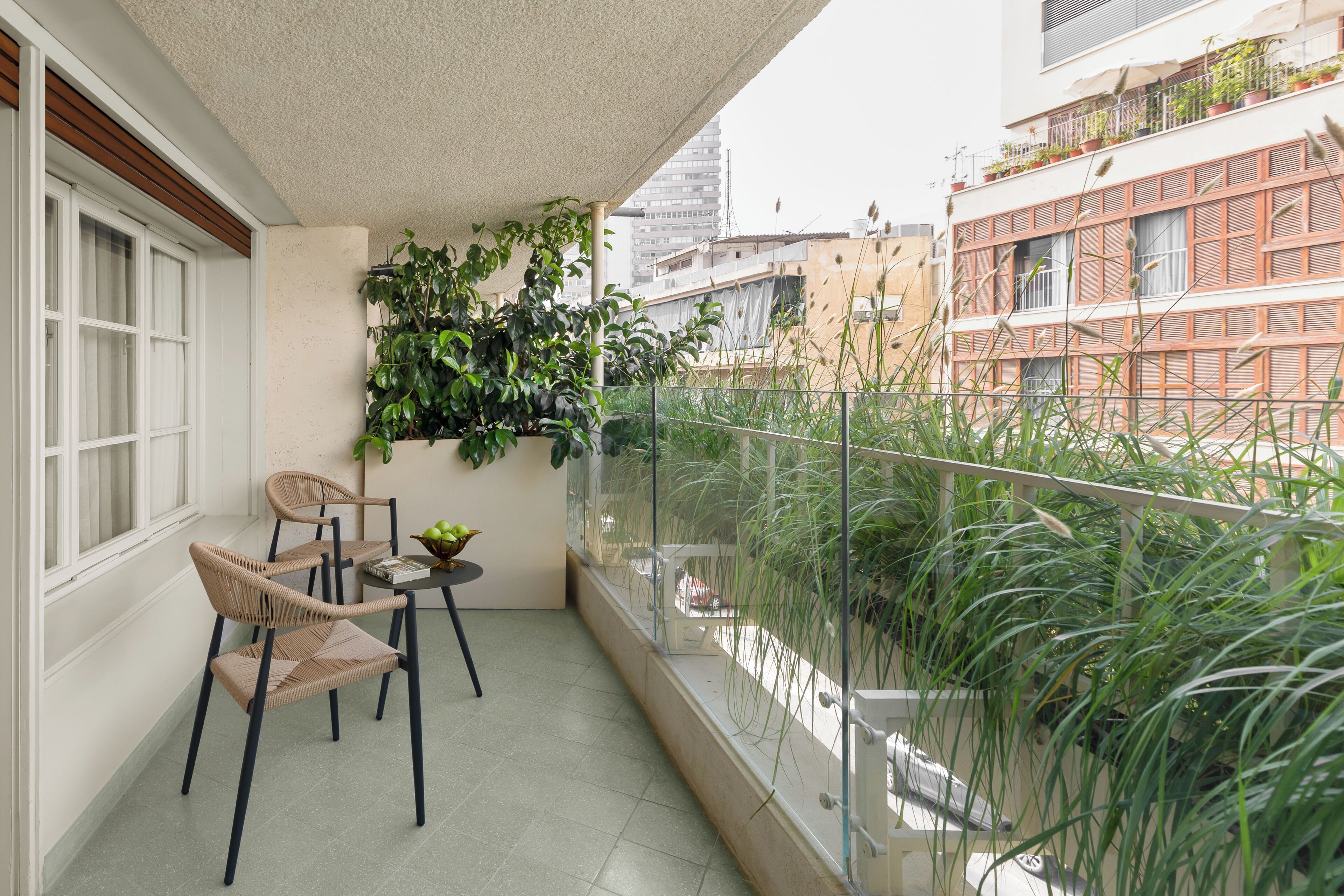 A balcony with two wicker chairs, a small table with a bowl of fruit, and a potted plant.