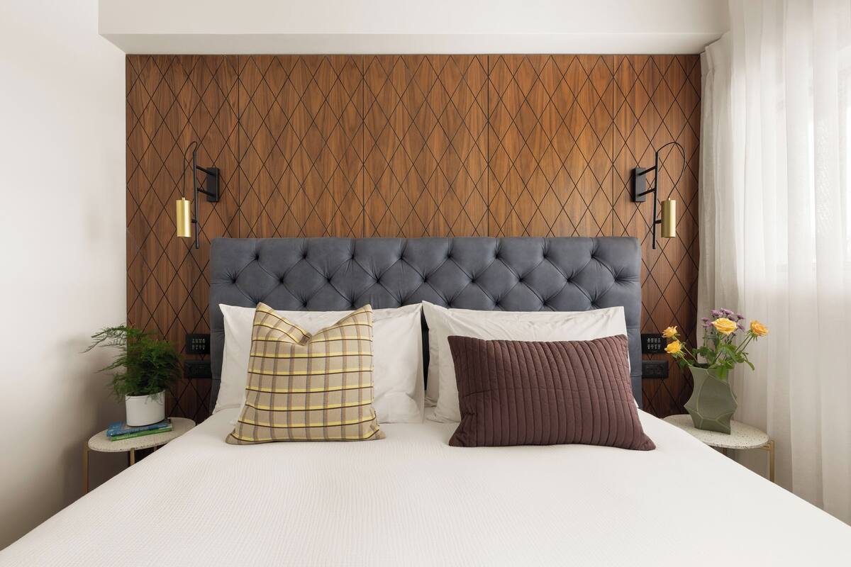 A bedroom with a tufted headboard, two bedside tables with lamps, and a nightstand with a plant.