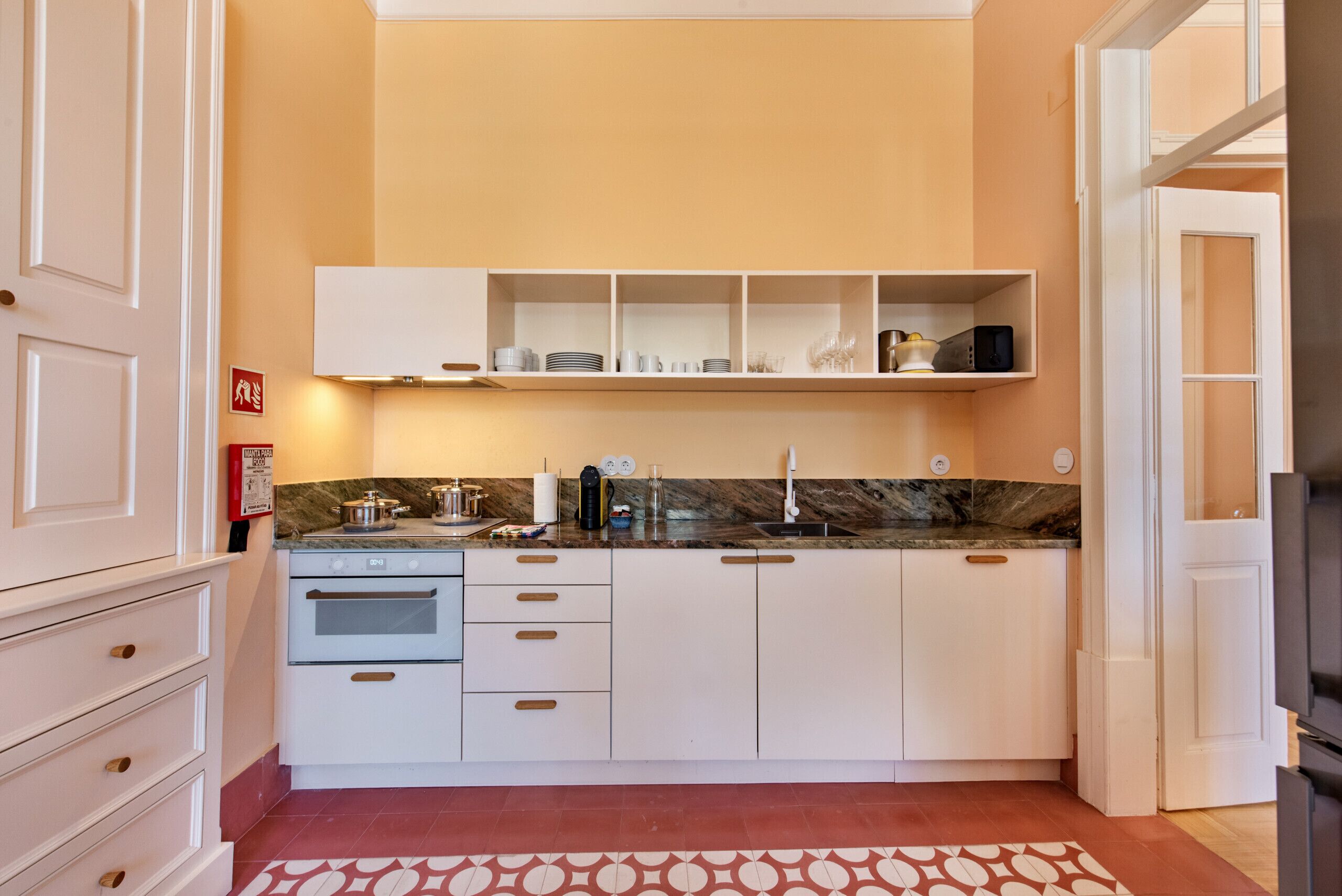 A modern kitchen with white cabinets, a marble countertop, and a patterned rug.