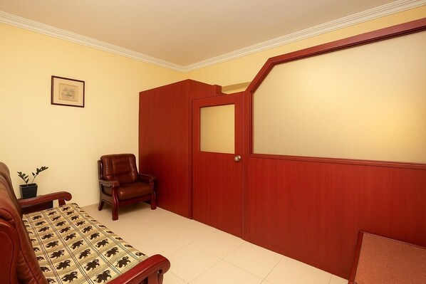 A room with a wooden door, a brown leather chair, a sofa with a patterned throw, and a framed picture on the wall. - Hotel Indraprastha Thiruvalla (Tiruvalla)