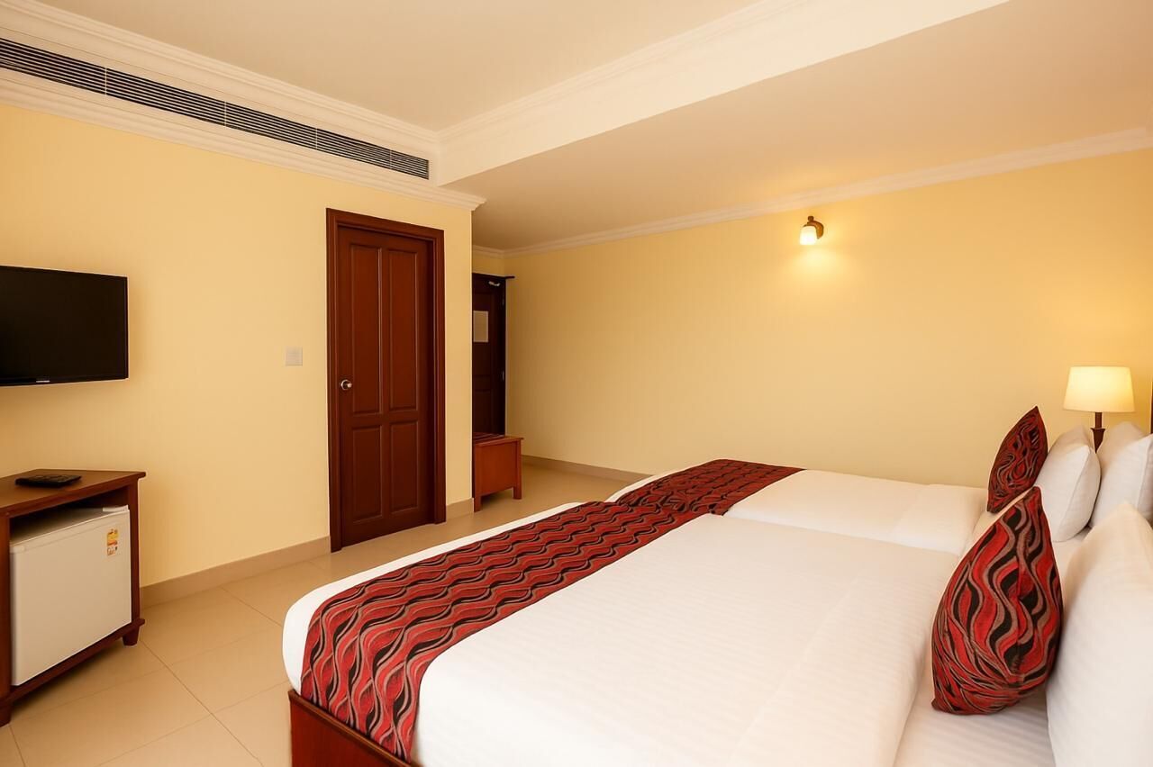 A hotel room with a bed, a TV, a desk with a refrigerator, and a door.