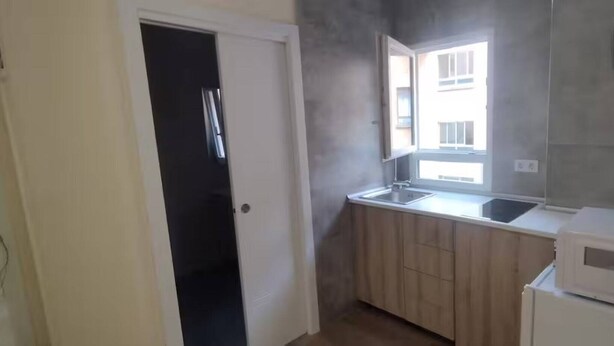 A small kitchen with wooden cabinets, a white refrigerator, and a window above the sink. - Studio for 3 people - Bilbao (Bilbao)