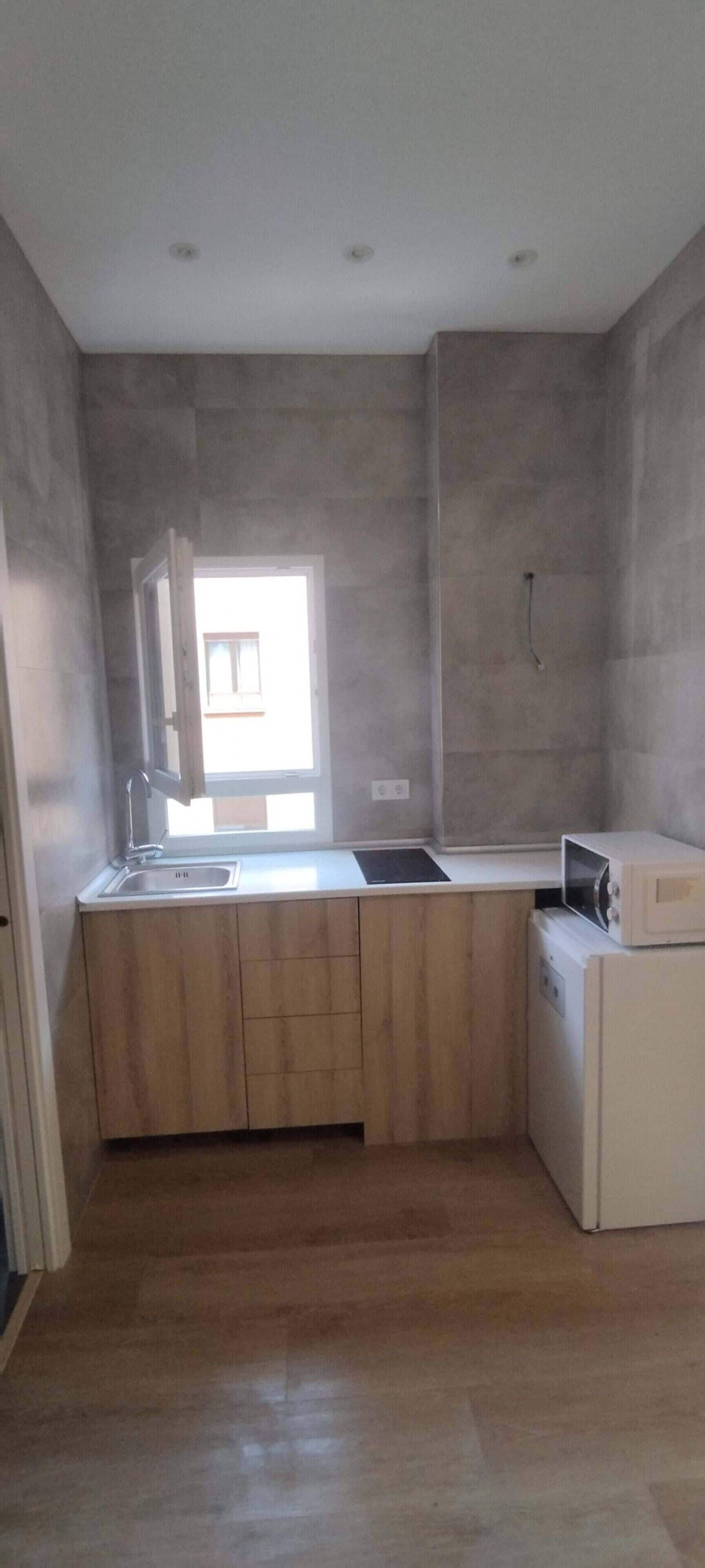 A compact kitchen with a built-in sink, a microwave, and wooden cabinetry.
