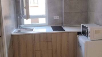 A compact kitchen with a built-in sink, a microwave, and wooden cabinetry.