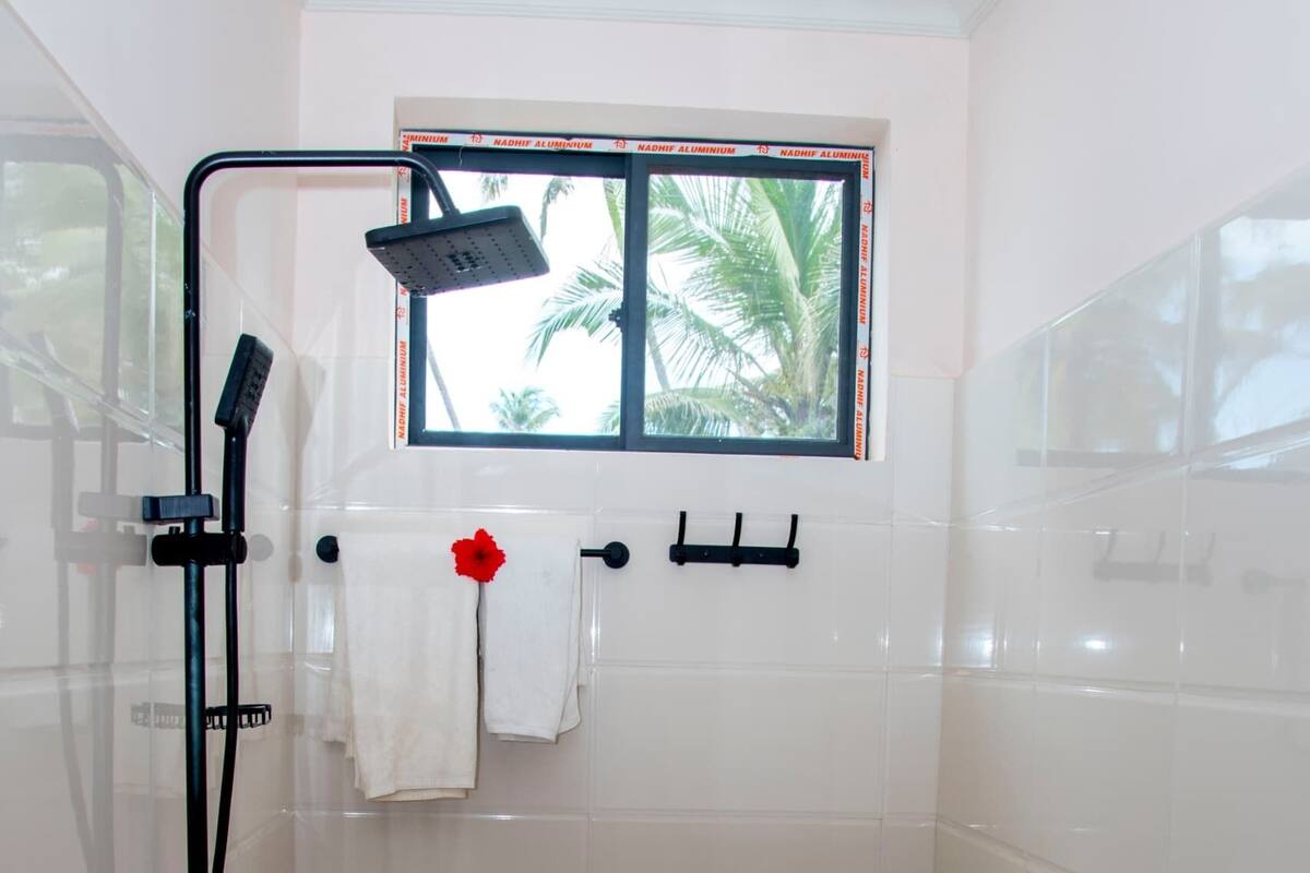A small bathroom with a toilet, a sink, and a shower. There is a window above the toilet, and towels are hanging on a rack.