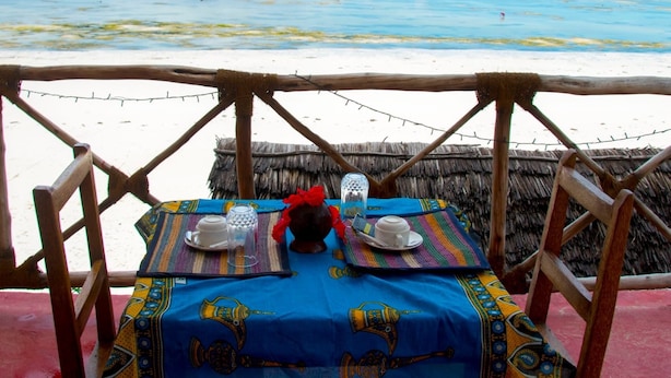 Une table dressée avec une nappe bleue et une assiette décorative, donnant sur une plage.