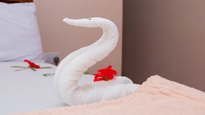 Une serviette en forme de cygne est posée sur un lit orné de fleurs rouges.