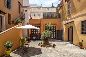 A courtyard with a central tree, potted plants, and a table with chairs. - Essence Collection Hotel (Rome)