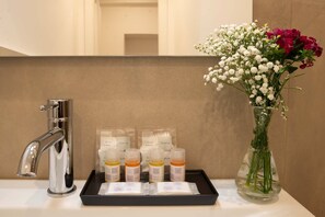 Uma bancada de banheiro com um dosador de touca de banho, um porta-objetos e um vaso de flores.