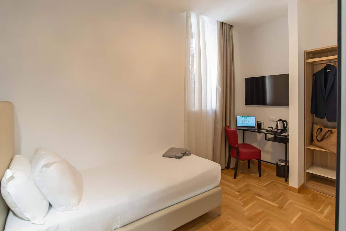 Una habitación de hotel con cama, escritorio con computadora, televisor y armario.