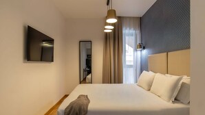 Une chambre d’hôtel avec un lit, un miroir, un luminaire suspendu et une vue sur un couloir.