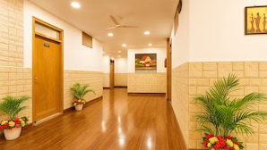 A hotel hallway with wooden flooring, potted plants, a ceiling fan, and a framed picture on the wall. - Hotel Shiva Lake - Near Mussoorie Lake (Mussoorie)