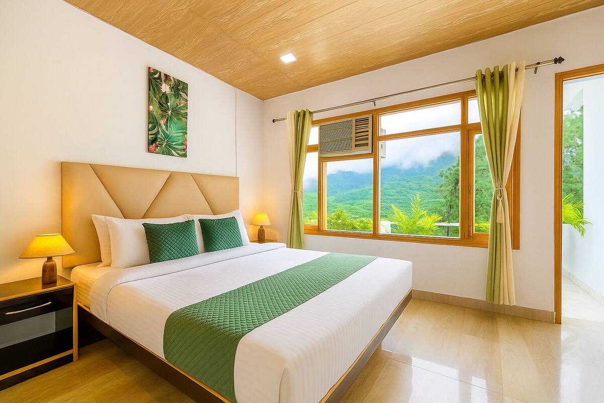 A hotel room with a large bed, wooden headboard, two bedside lamps, a window with curtains, and a view of greenery outside.