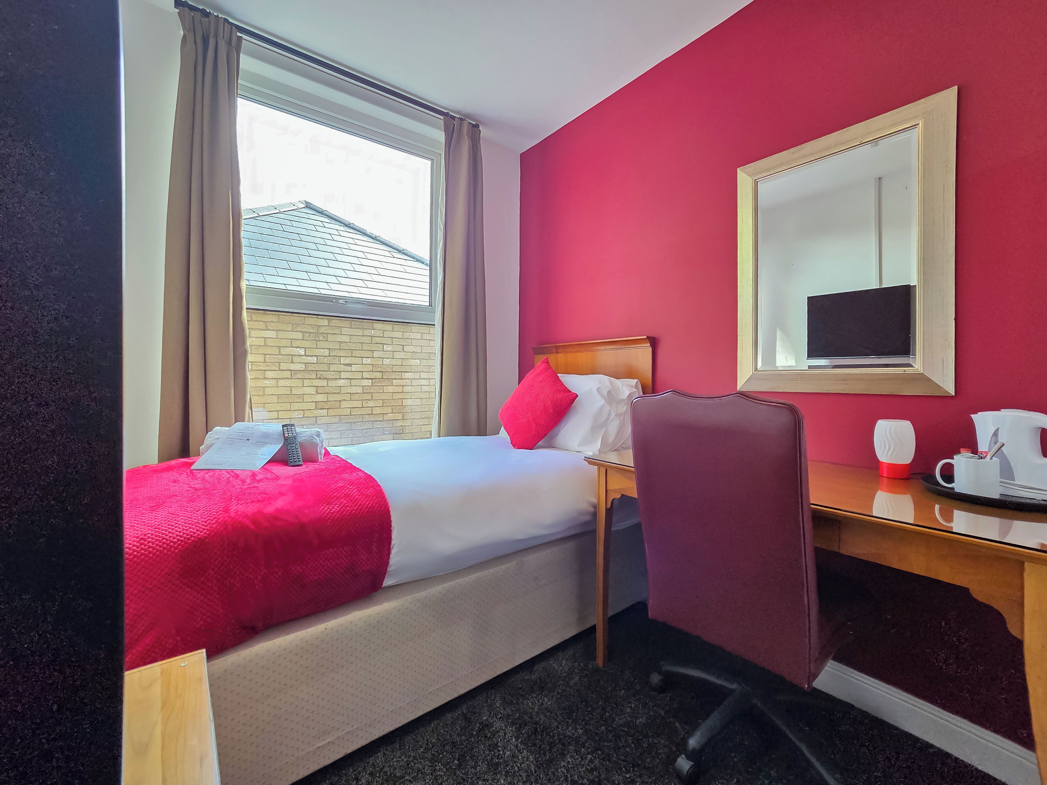 A hotel room with a bed, a desk, a chair, a coffee maker, and a window with curtains.
