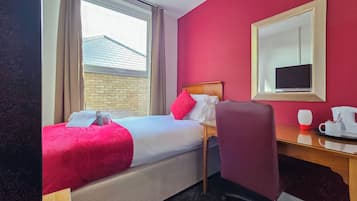 A hotel room with a bed, a desk, a chair, a coffee maker, and a window with curtains.