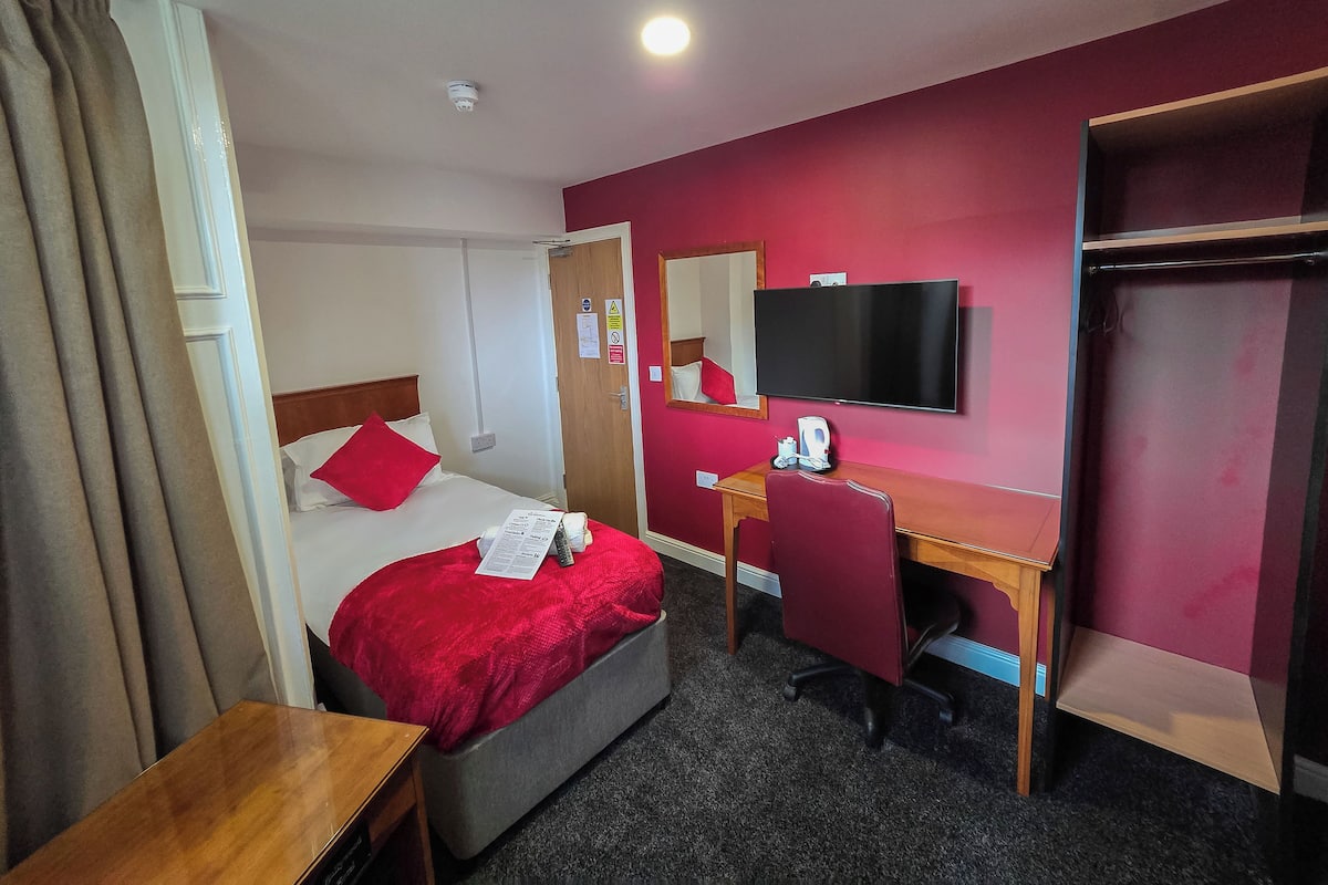 A hotel room with a bed, a desk, a chair, a television, and a wardrobe.