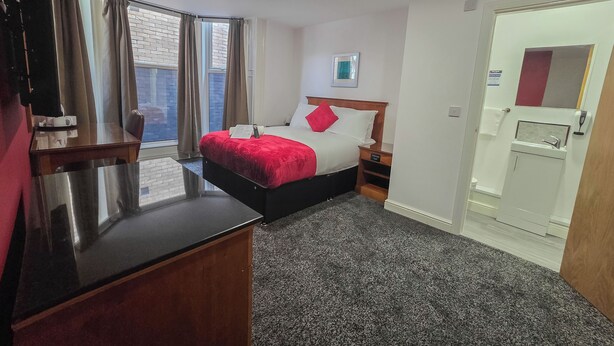 A hotel room with a bed, bedside table, and a small desk. - Hullywood Rooms (Hull)