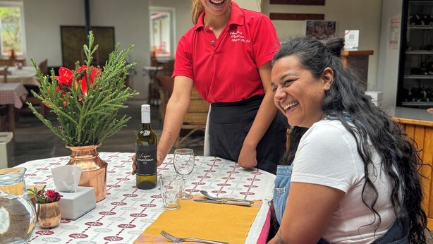 Une table dressée avec une nappe à motifs, une bouteille de vin et un vase rempli de fleurs rouges.