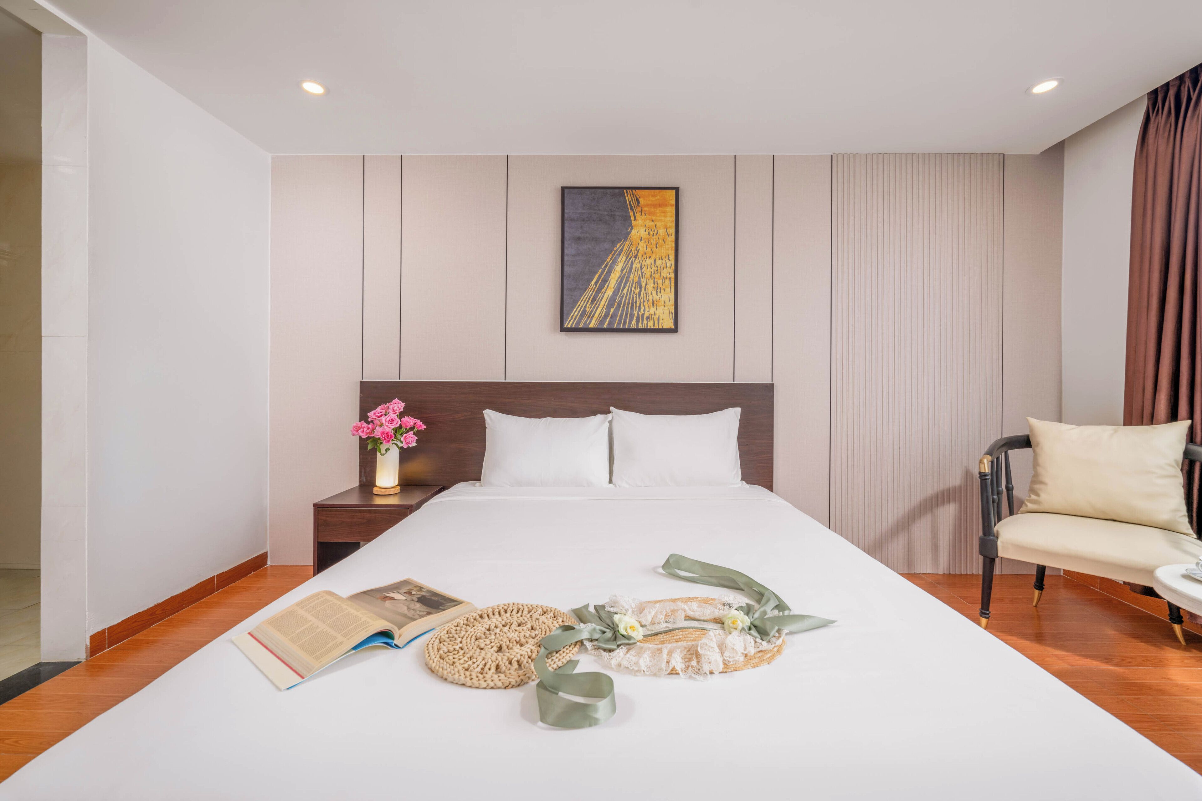 A neatly made bed with a pillow, a bedside table with a vase of flowers, a chair, and a framed picture on the wall.