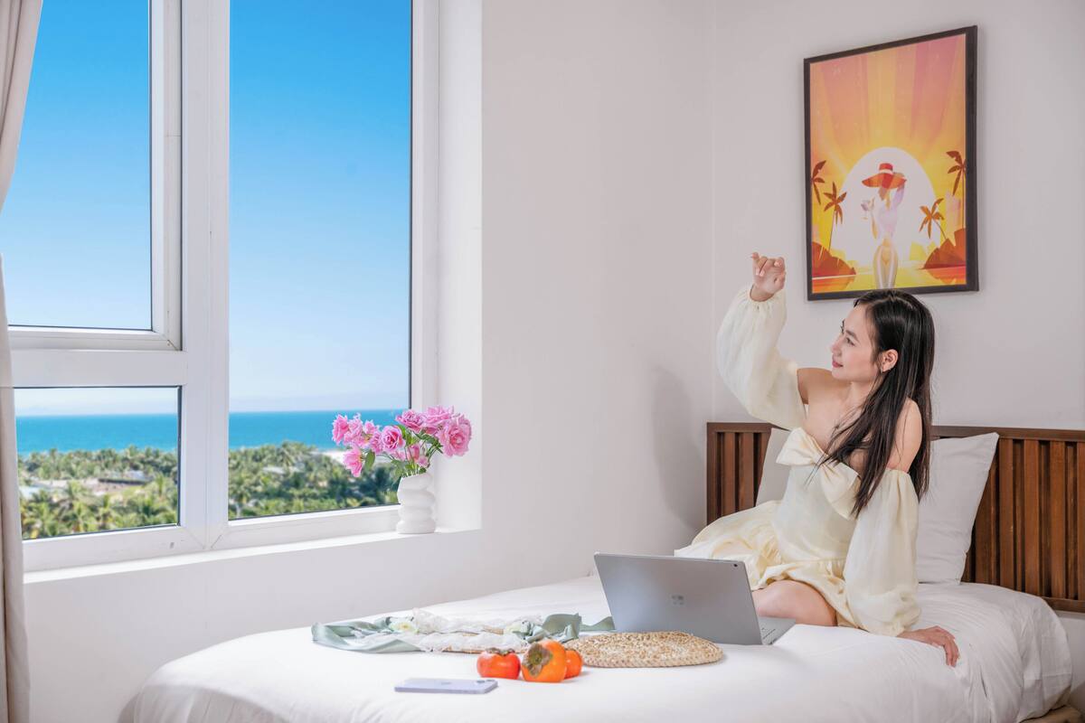 A room with a bed, a laptop, a smartphone, and a vase with flowers.