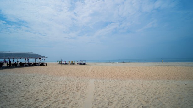 A beach with a covered seating area and a clear sky. - Ocean Whisper Goa (Goa)