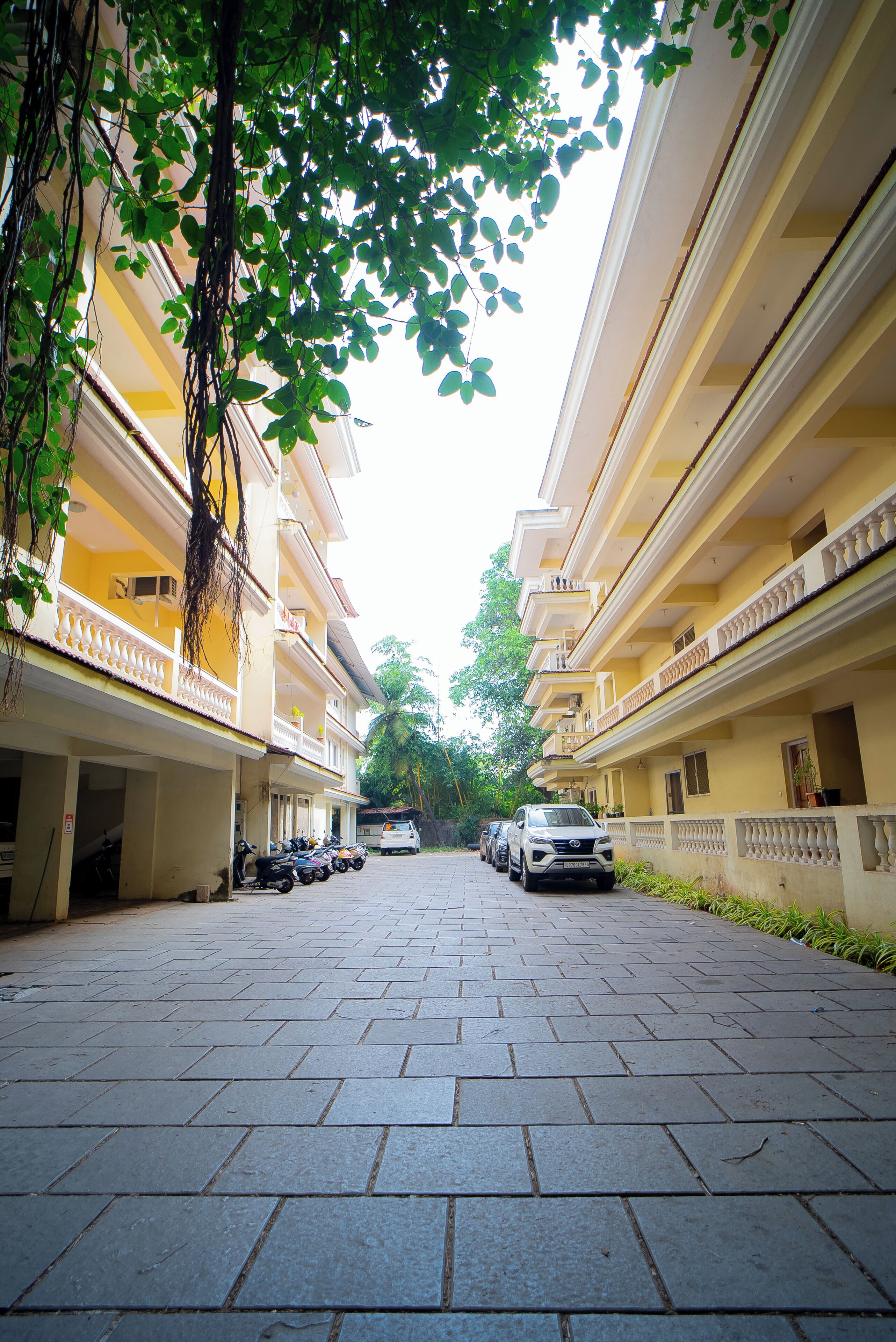 A multi-story building with a paved walkway, balconies, and parked vehicles.
