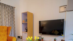 A modern living room with a sofa, a coffee table with a vase of flowers, a TV, and a bookshelf. - Ocean Whisper Goa (Goa)