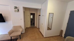 Een woonkamer met een beige fauteuil, een tafeltje en een televisie. Een gang leidt naar een badkamer.