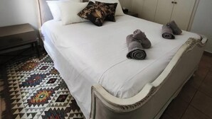 Een slaapkamer met een bed, kussens, een kamerkleed met patroon en een kledingkast.