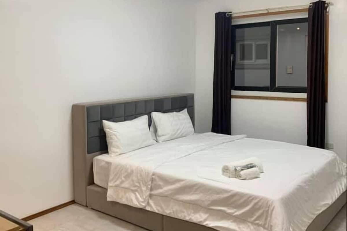 A modern hotel room with a large bed, a bedside table, and a window with curtains.