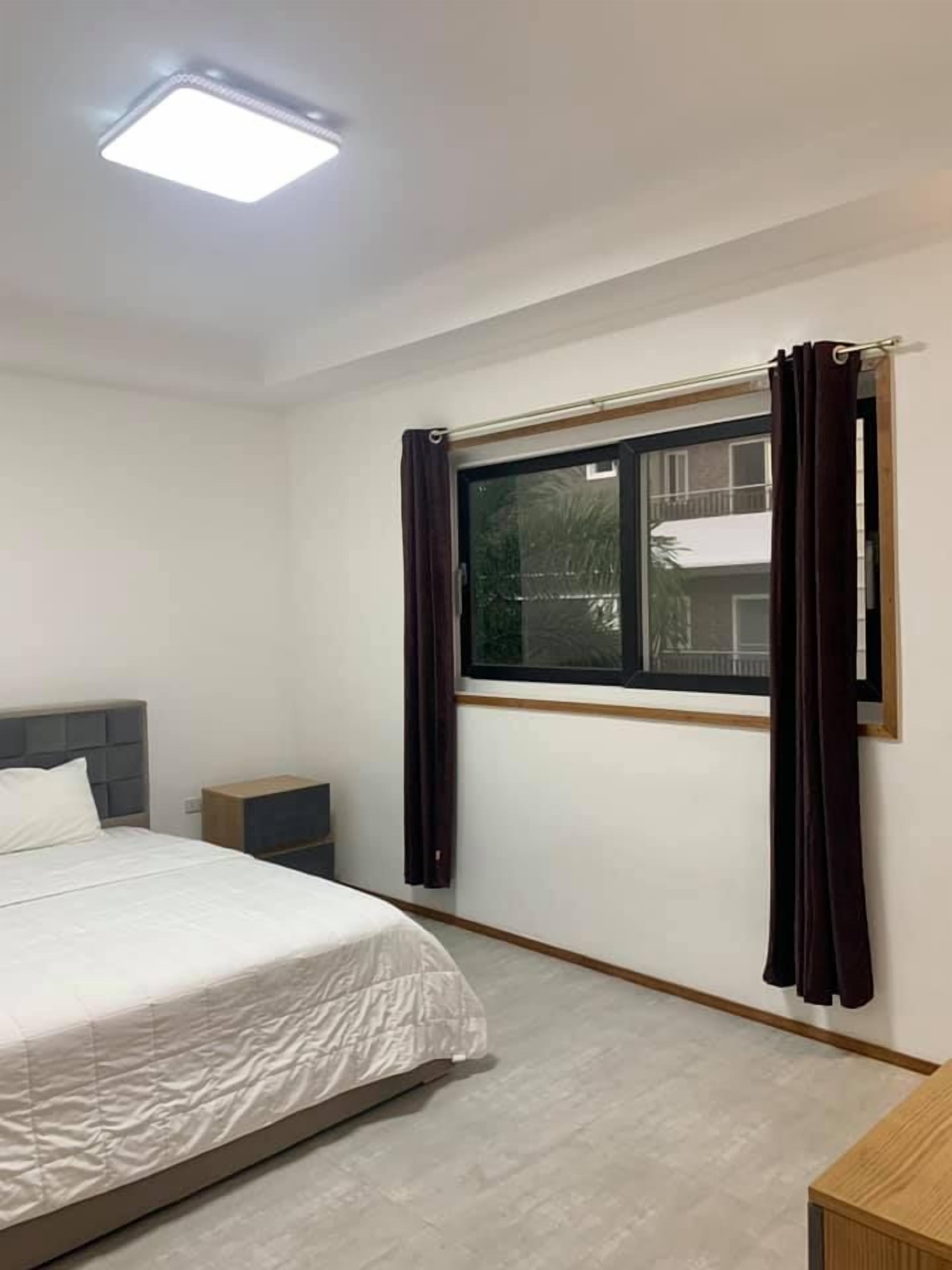 A bedroom with a bed, a nightstand, a window with curtains, and a ceiling light.