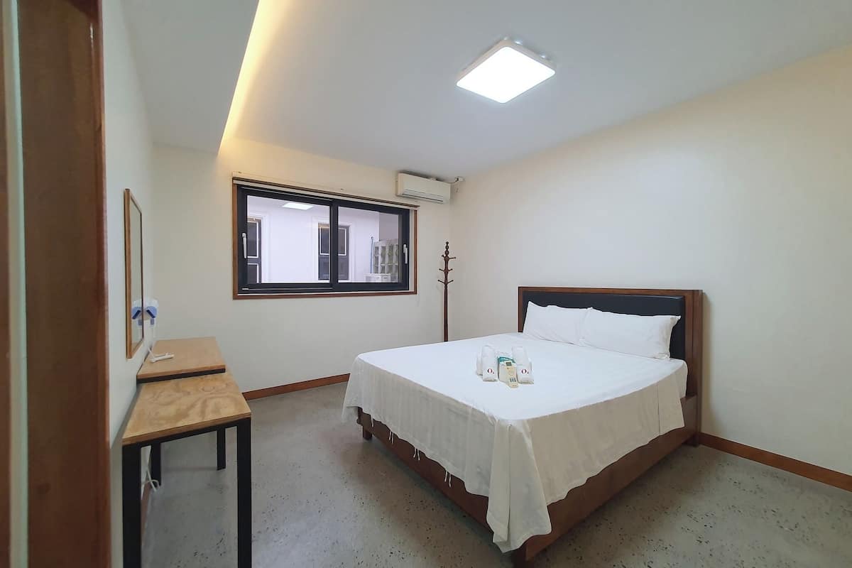 A hotel room with a bed, a small table, a window, and an air conditioning unit.