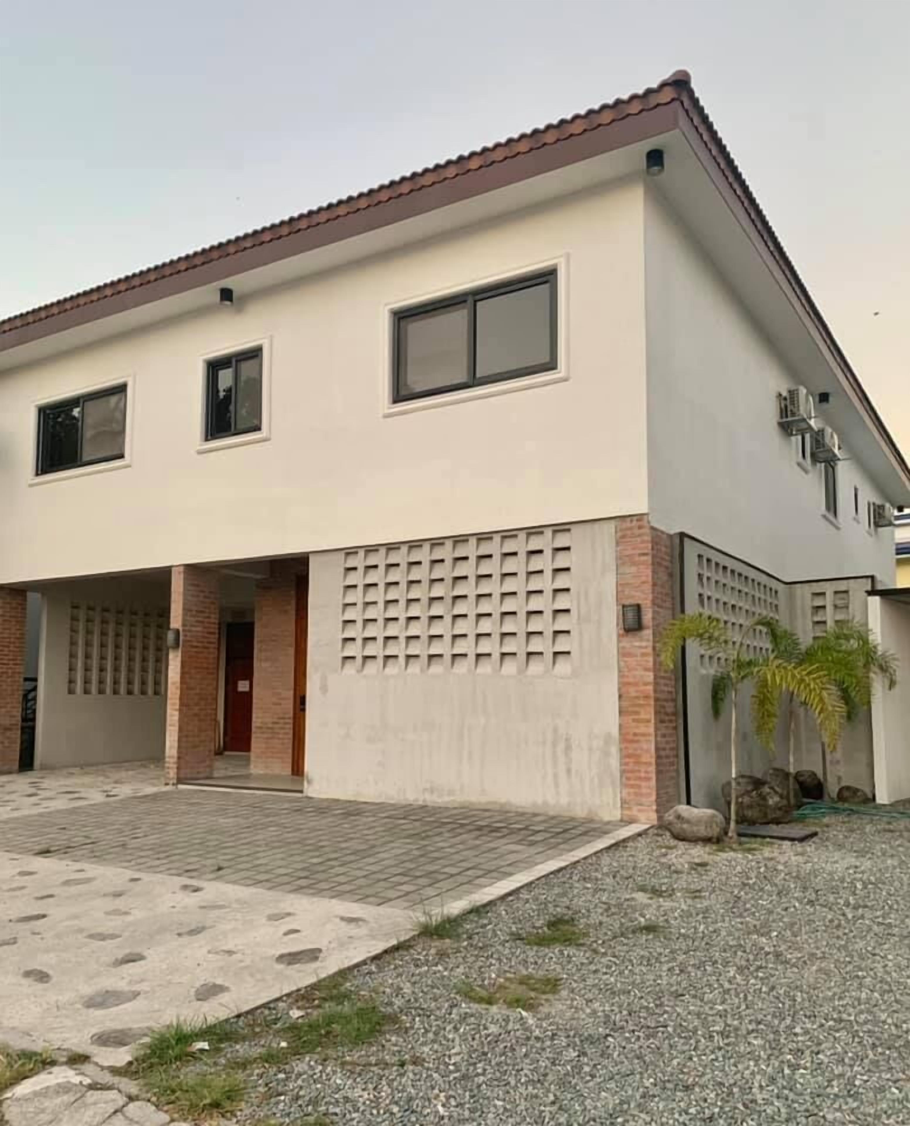 A two-story house with a tiled driveway, a garage, and a small garden with palm trees.