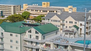 A coastal hotel with multiple balconies, a swimming pool, and a view of the ocean. - Aventurra 403 — Modern Beach Block Penthouse Oasis with Rooftop Pool, Bay Views & Walkable Fun — Sleeps 9 (Ocean City)